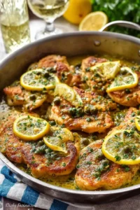 Golden chicken piccata fillets in a lemon butter sauce with capers and fresh parsley served in a skillet.