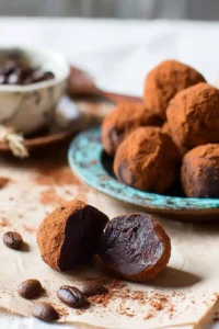 Close-up of rich coffee chocolate truffles dusted with cocoa powder, served with coffee beans and a cup of espresso.