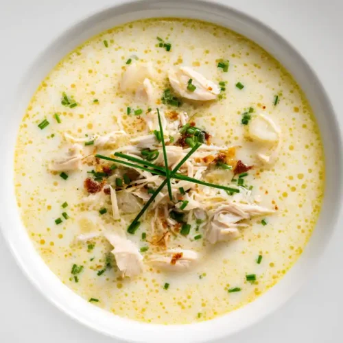 creamy chicken soup recipe with tender chicken pieces, herbs, and chives served in a white bowl