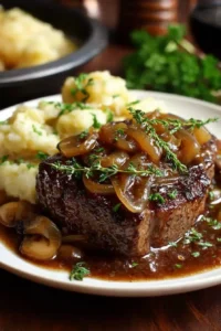Close-up of crockpot cube steak topped with caramelized onions and rich brown gravy served with mashed potatoes.