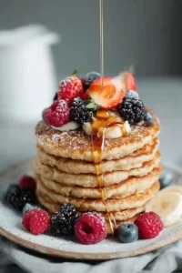 Stack of fluffy pancakes topped with strawberries, raspberries, blackberries, and maple syrup drizzle