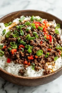 Bowl of Korean ground beef served over steamed white rice with sesame seeds, chopped red peppers, and green onions