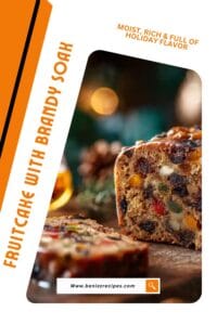 Close-up of a moist Christmas fruitcake with colorful dried fruits and nuts, topped with a shiny rum glaze on a rustic wooden board with festive lights in the background.