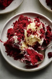 A close-up of a moist red velvet cake slice topped with creamy frosting on a white plate.