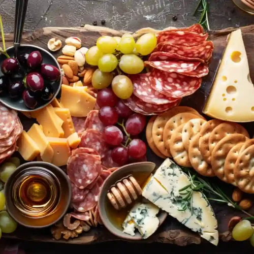 Overhead shot of an elegant charcuterie board with assorted cheeses, cured meats, grapes, crackers, and honey