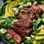 Juicy sliced steak served over spinach with creamy blue cheese and avocado slices