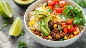 Taco rice bowl with seasoned beef, avocado, corn, tomatoes, and cilantro served with lime