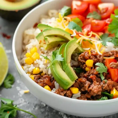 Taco rice bowl with seasoned beef, avocado, corn, tomatoes, and cilantro served with lime