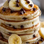 Delicious banana chocolate chip pancakes stacked on a plate, topped with syrup