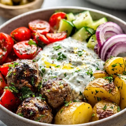 A colorful Greek Meatball Bowl with meatballs, fresh vegetables, and herbs.