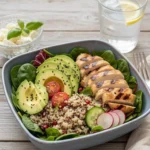 Healthy chicken avocado quinoa bowl topped with fresh herbs and vegetables