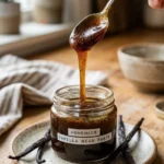 Homemade vanilla bean paste in a jar with vanilla beans and measuring spoon.