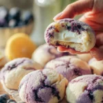 Lemon blueberry cheesecake cookies on a plate, topped with fresh blueberries.
