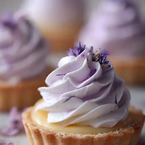Mini lemon tart topped with lilac meringue on a decorative plate.