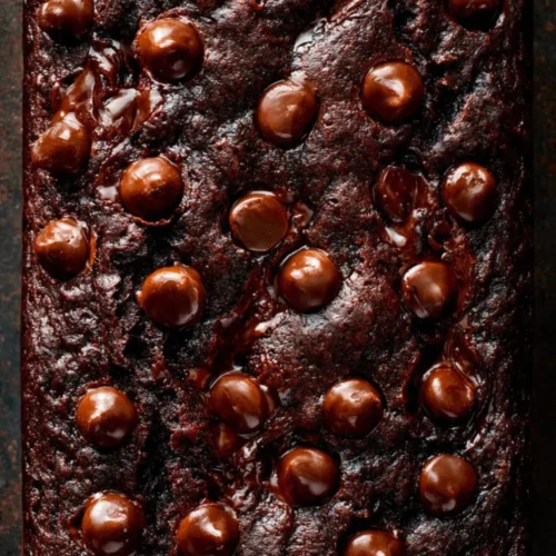 Slice of chocolate zucchini bread with chocolate chips and zucchini on a plate.